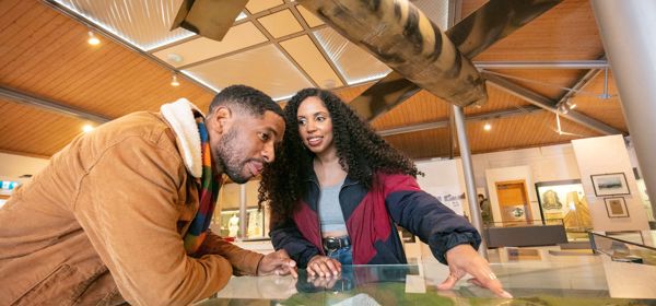 A couple leaning over an exhibition case inside a museum.