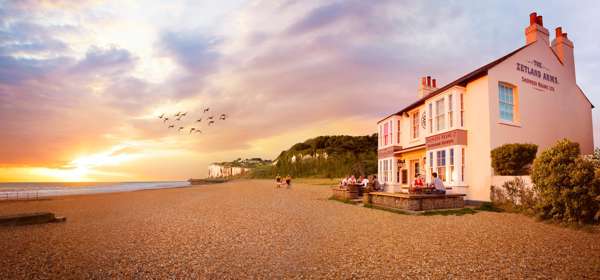 The Zetland Arms located on a pebble beach with cliffs in the background.