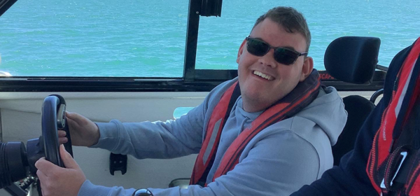 A smiling man in a wheelchair piloting a boat.